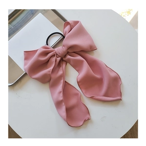 Close-up of a pink fabric bow hair tie with a long ribbon detail on a white surface