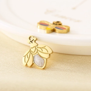 Macro shot of gold bee charm with carved wings and white enamel inlay on ivory fabric