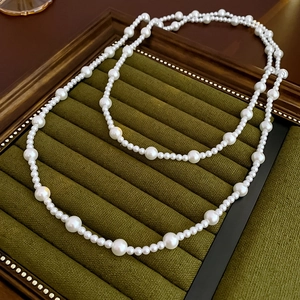 Macro view of a long double-layer pearl necklace on a green velvet jewelry display tray