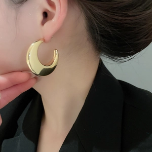 Close-up of model wearing thick gold C-shaped metal hoop earrings with high mirror finish