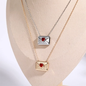 Detail showing gold and silver envelope necklaces with red heart stones on a beige bust