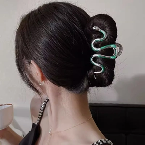 Detail view of silver snake-shaped hair claw with green enamel worn in a stylish updo hairstyle