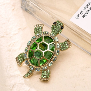 Close-up of a golden turtle brooch with green crystals and faceted emerald-tone stones