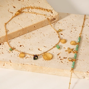 Close-up of 18K gold starfish and shell charms with green natural stones on the chain