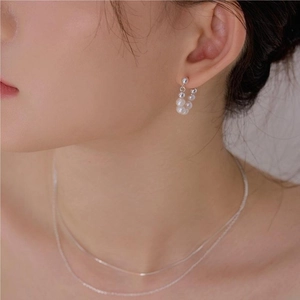 Close-up of elegant pearl drop earrings and layered silver necklace on a female model