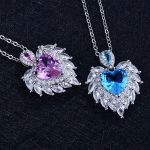 Detailed close-up of pink and blue heart-shaped angel wing necklaces on black fabric