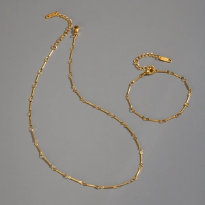 Detail of 18K gold plated bone-link chain necklace and bracelet set on a grey background