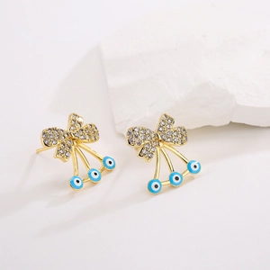 18K gold plated bow earrings with zircon and blue evil eye charms on a white stone