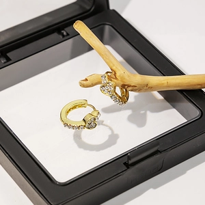 Détail de boucles d'oreilles cœur dorées avec strass blancs sur un décor en bois d'art
