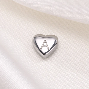 Close-up of heart-shaped stainless steel bead with engraved letter A on white silk