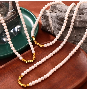 Detailed close-up of pearl necklace with gold sugar cube beads on vintage stone