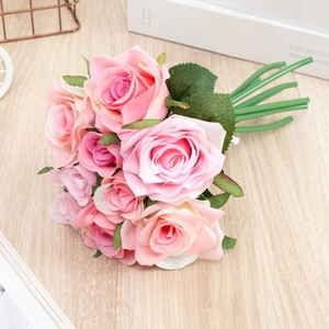 Close-up of realistic pink artificial rose bouquet on light wood background with metal basket