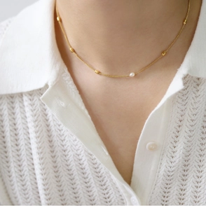 Close-up of elegant 18K gold-plated necklace with oval beads and a round pearl on neck