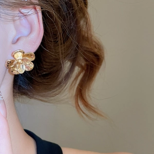 Close-up of a model wearing elegant gold floral earrings with a smooth polished finish