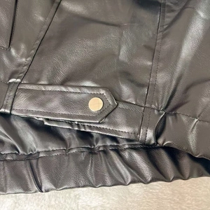 Détail du bord de la veste en cuir PU noir avec boutons-pression en métal argenté