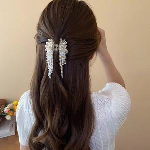 Detailed view of artificial pearl tassel hair claw clip worn on wavy brown hair