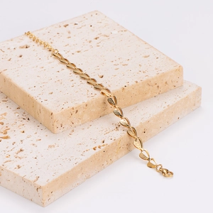 Minimalist gold leaf charm bracelet displayed on elegant travertine stone background