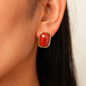 Gros plan sur une boucle d'oreille rétro dorée avec pierre en résine rouge et relief