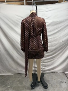 Vista posteriore di un abito in chiffon marrone a pois con collo alto e bordo in pelliccia