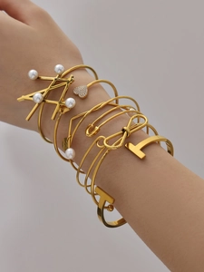 Close-up of stacked gold-plated bracelets featuring heart charms and pearl accents