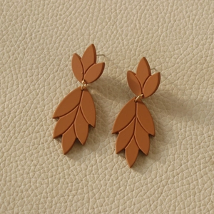 Detailed view of caramel leaf-shaped matte clay earrings on white leather background