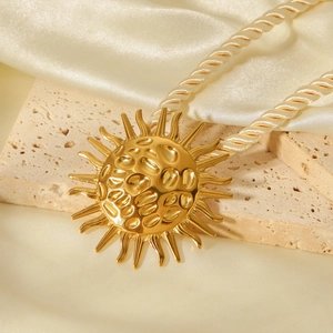 Detail view of a hammered texture gold sun pendant on a twisted rope chain over silk
