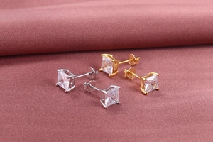 Close-up of gold and silver S925 silver square zircon stud earrings on soft fabric