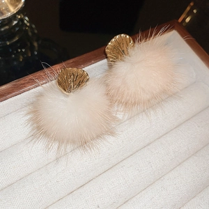 Detail of elegant gold fan-shaped metal earrings with soft beige plush pompom drops