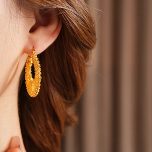 Gros plan d'une boucle d'oreille créole dorée à texture tressée portée par un mannequin
