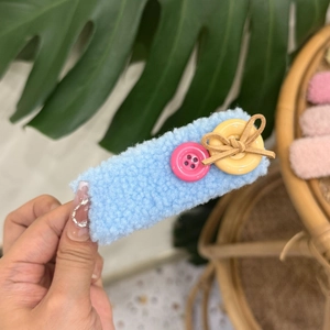 Macro detail of a light blue plush teddy hair clip with pink and yellow button accents