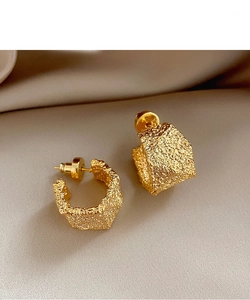 Macro shot of gold-plated C-shaped earrings with irregular pleated texture on silk