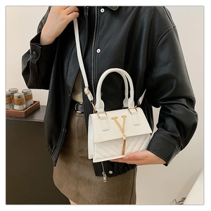 Close-up of white crossbody bag with quilted pattern, gold V-clasp and fringe detail