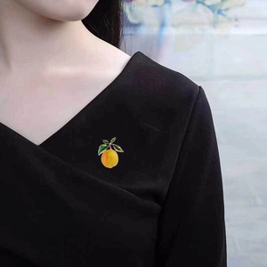 Detailed view of an enamel persimmon fruit brooch pinned on a black V-neck garment