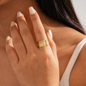 Detail of a wide gold stacked ring with multilayered metallic texture on a model's hand