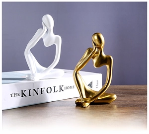 Detail of Nordic abstract thinker statues in matte white and metallic gold on wooden desk