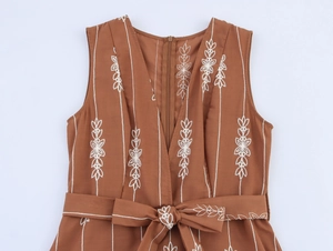 Détail d'une robe col V caramel avec broderie florale blanche et nœud à la taille