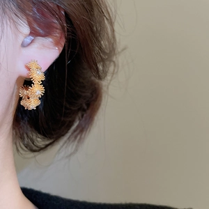 Detail of gold floral C-shape stud earrings with zircons shown on model ear