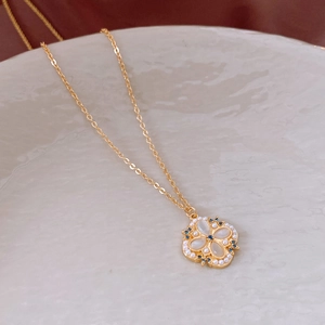 Detailed close-up of gold clover pendant with mother of pearl and small blue crystals