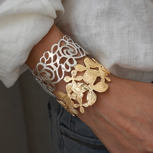 Minimalist wide metal cuff bracelets with floral patterns worn by a model in casual style