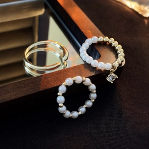 Detailed view of a 3-piece gold-plated pearl and zircon ring set on a mirror surface
