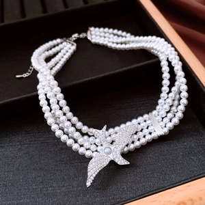 Detail of four-row pearl necklace featuring a diamond-studded bird pendant in a jewelry tray