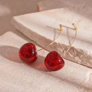 Detailed view of red resin cherry earrings with gold hooks and sparkling glitter details