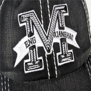 Close-up of white letter M embroidery on a washed black denim baseball cap detail
