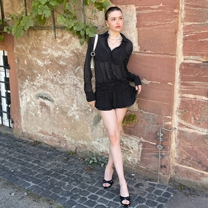 Dettaglio ravvicinato di una tutina nera in chiffon a pois con colletto a polo e maniche lunghe