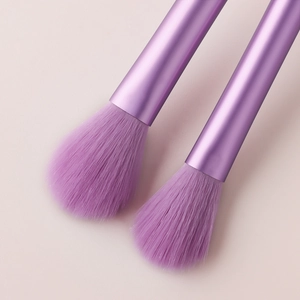Close-up of two mini purple makeup brushes with soft bristles on a pink background