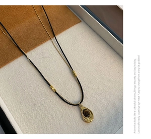 Detail of water drop tiger eye pendant on a double-layer black leather and gold chain