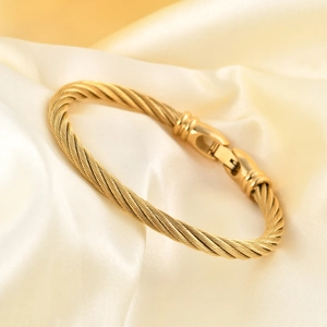 Elegant gold twisted cable stainless steel bangle featuring a secure clasp on silk fabric