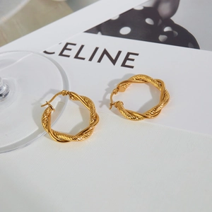 Detailed view of gold twisted hoop earrings placed on a minimal white aesthetic surface