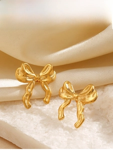 Macro shot of gold 18K plated bow earrings with lava texture on silk background