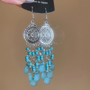 Detail view of silver tassel earrings with blue beads and sunflower pattern on black card